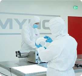 Workers in protective suits in a cleanroom environment handling equipment.
