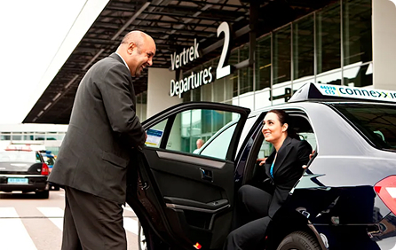 Chauffeur helpt een vrouw in een taxi bij een luchthaven