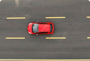 Aerial view of a red car driving on a road with lane markings